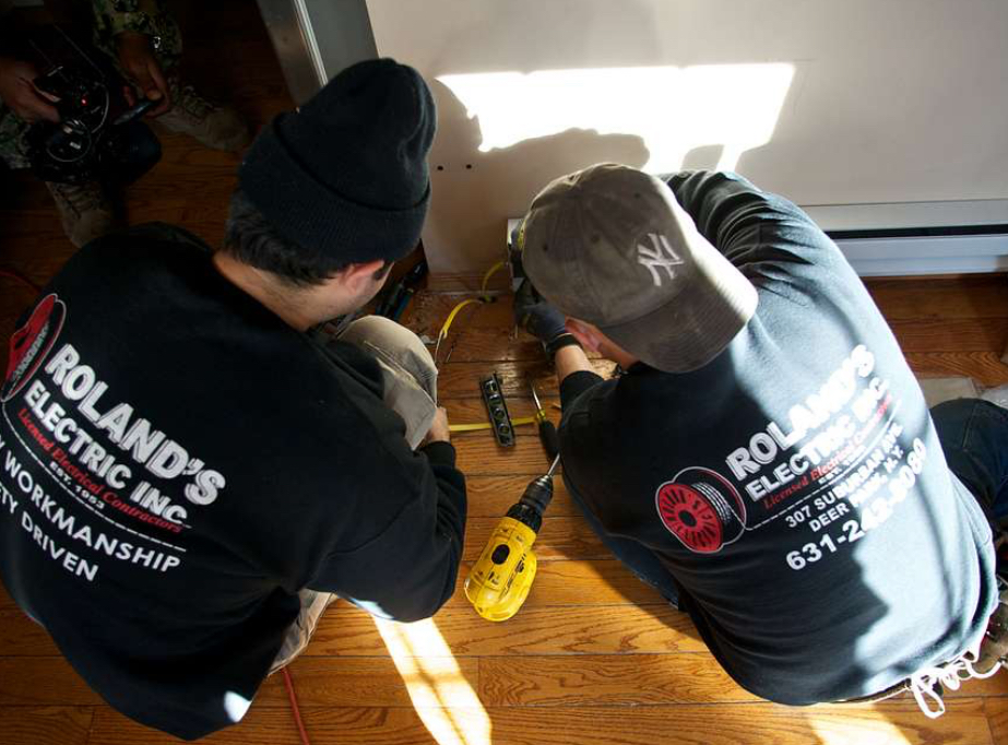 Two electricians working on wiring inside a domestic wall frame